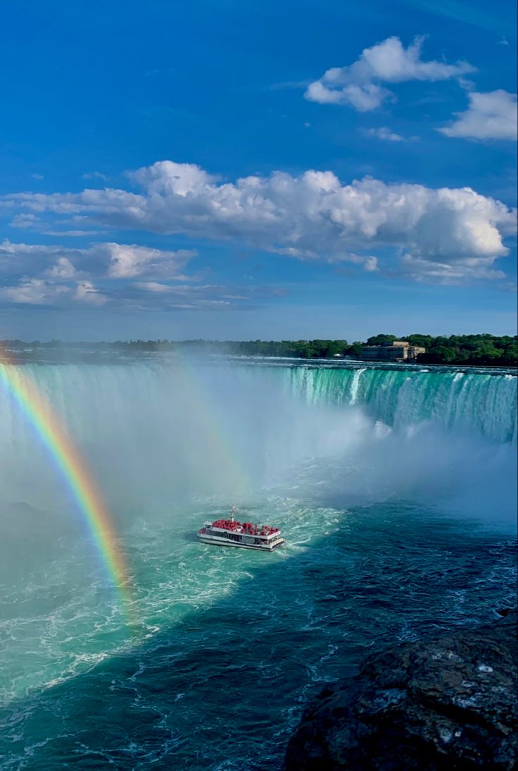 a boat is in the water with a rainbow above it and a waterfall behind it