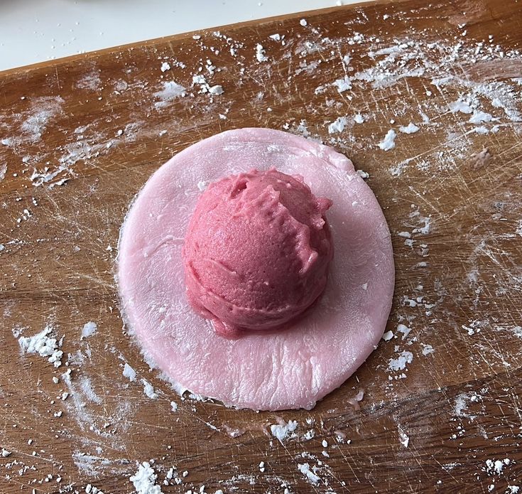 a pink doughnut sitting on top of a wooden cutting board