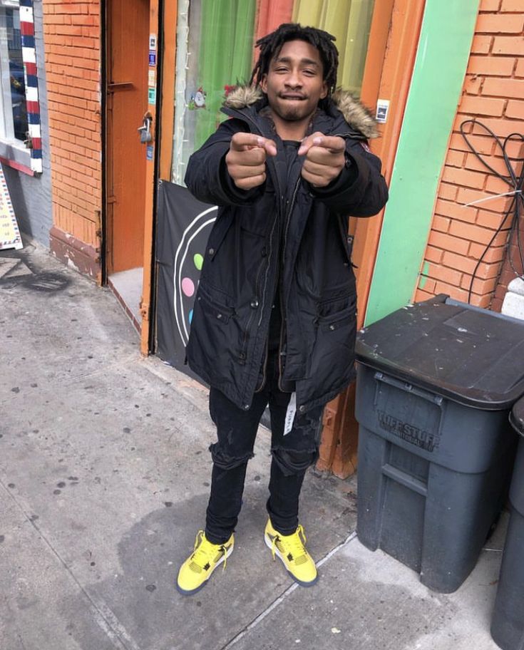 a man with dreadlocks standing in front of a building giving the thumbs up