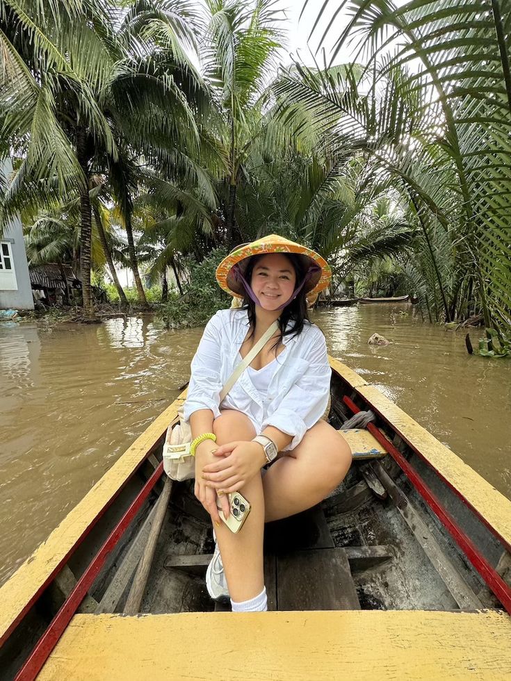 a woman in a straw hat is sitting on a boat with palm trees behind her