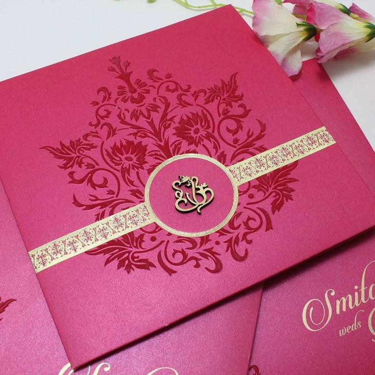 two pink and gold wedding cards on a table