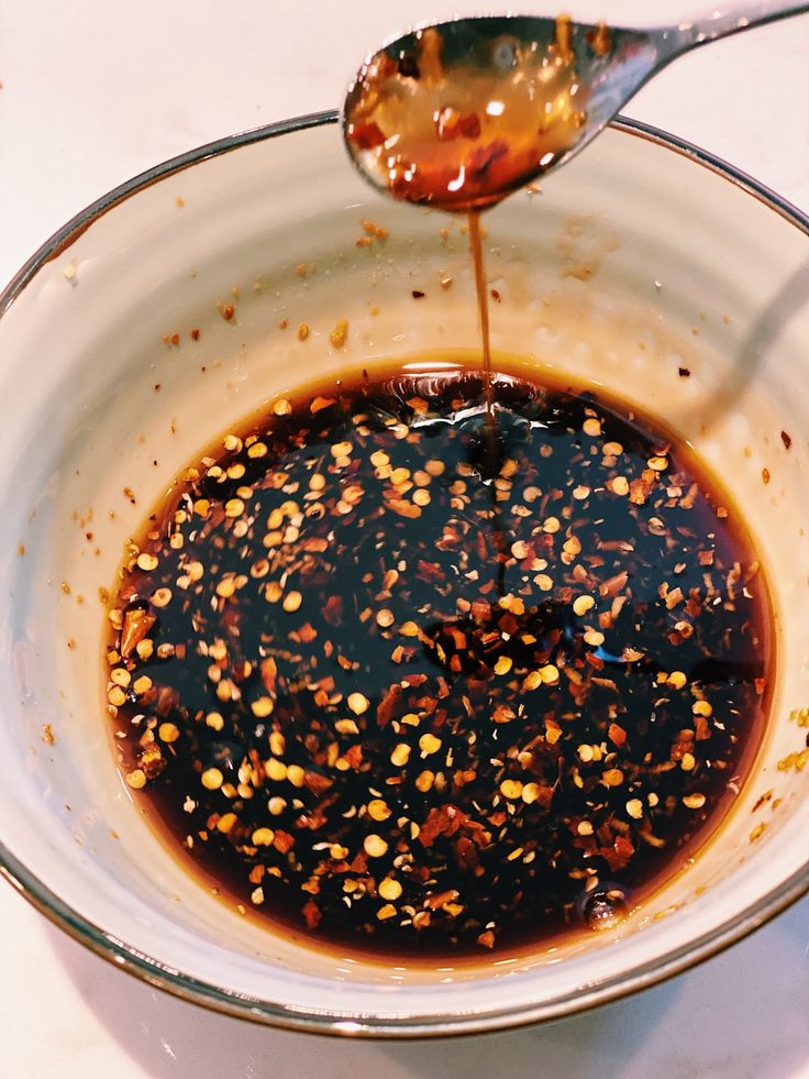 a spoon pouring sauce into a bowl filled with condiments