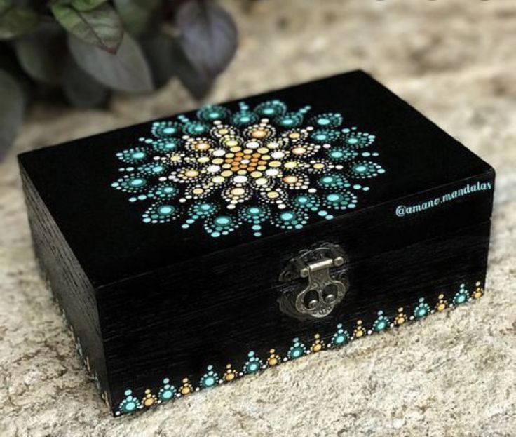 a small wooden box with beaded designs on the lid sitting on a table next to a plant