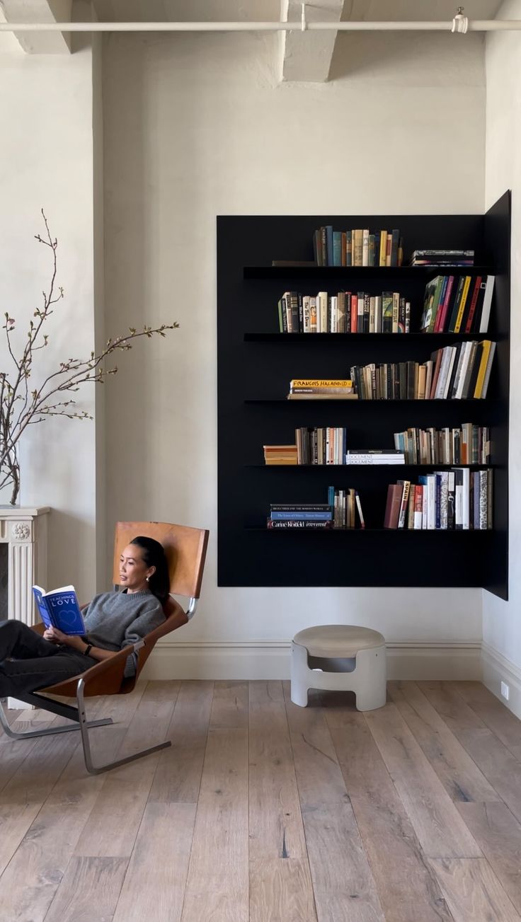 a woman sitting in a chair with a book case on the wall next to her