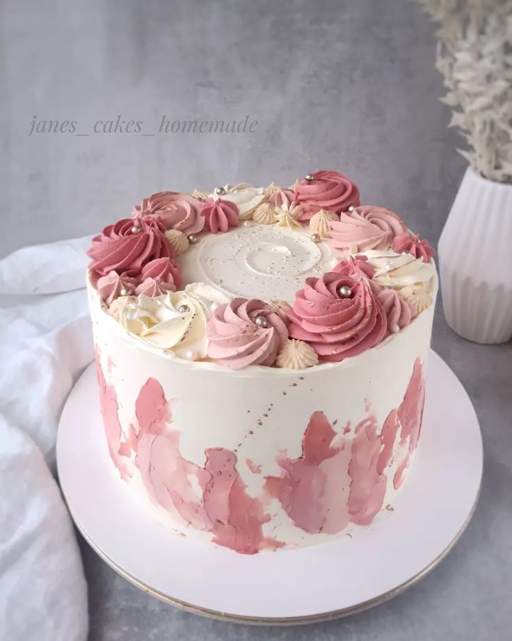 a white cake with pink frosting and flowers on the top is sitting on a plate