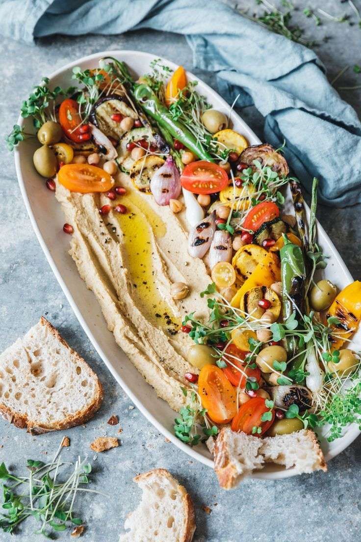 a platter filled with bread and vegetables on top of a gray tablecloth next to some slices of bread