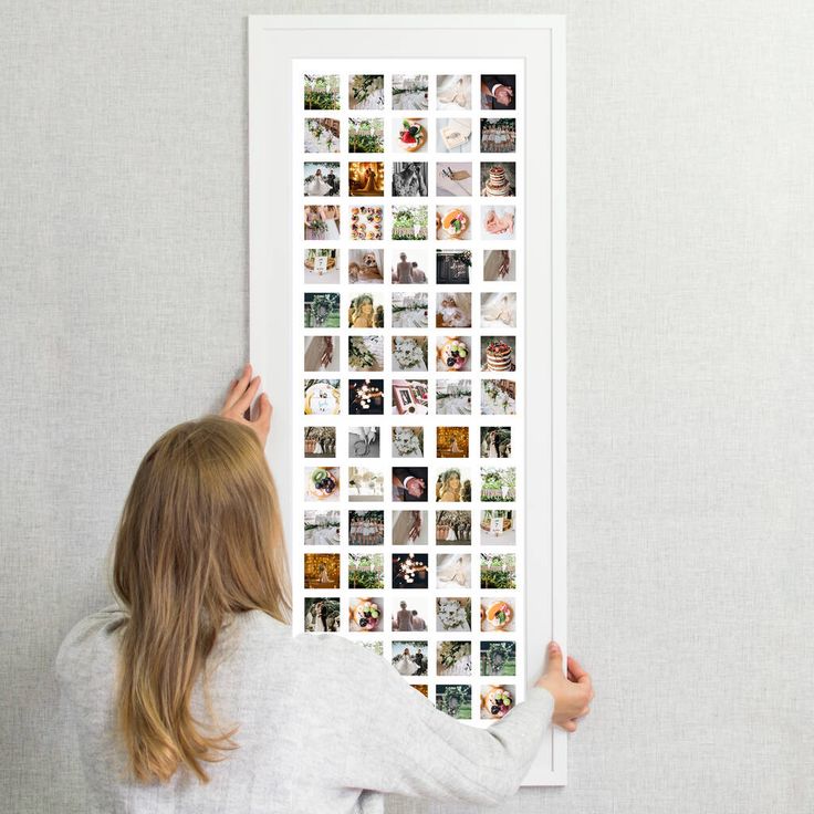 a woman is holding up a large poster with pictures on the wall in front of her