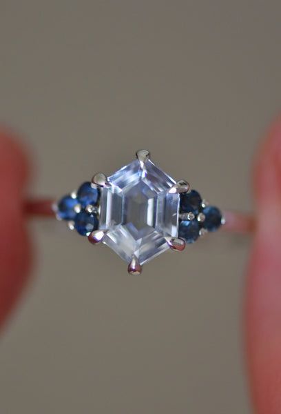 someone is holding a ring with an emerald and blue sapphire