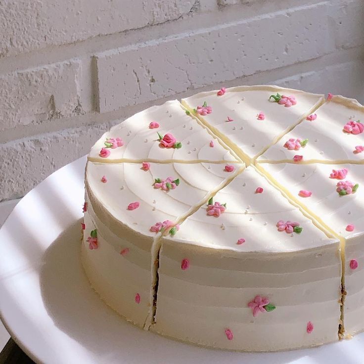 a white cake with pink flowers on it sitting on a plate next to a brick wall