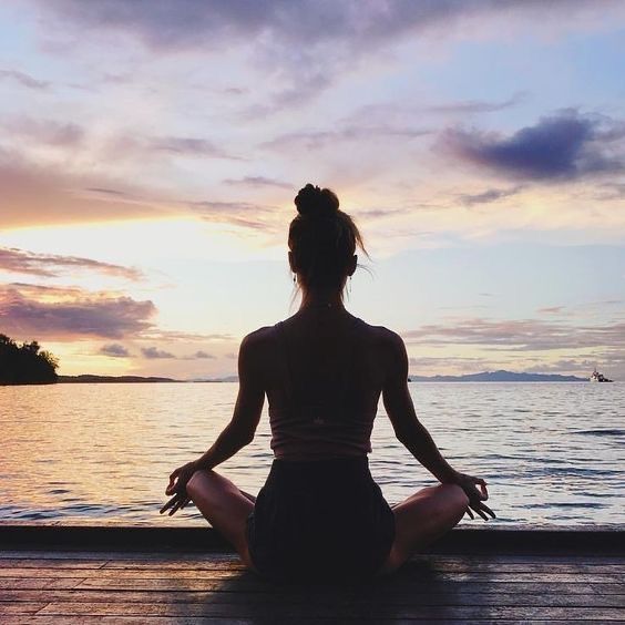 a woman is sitting in the middle of a yoga pose by the water at sunset