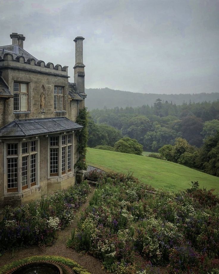 an old stone house in the middle of a lush green field with lots of flowers