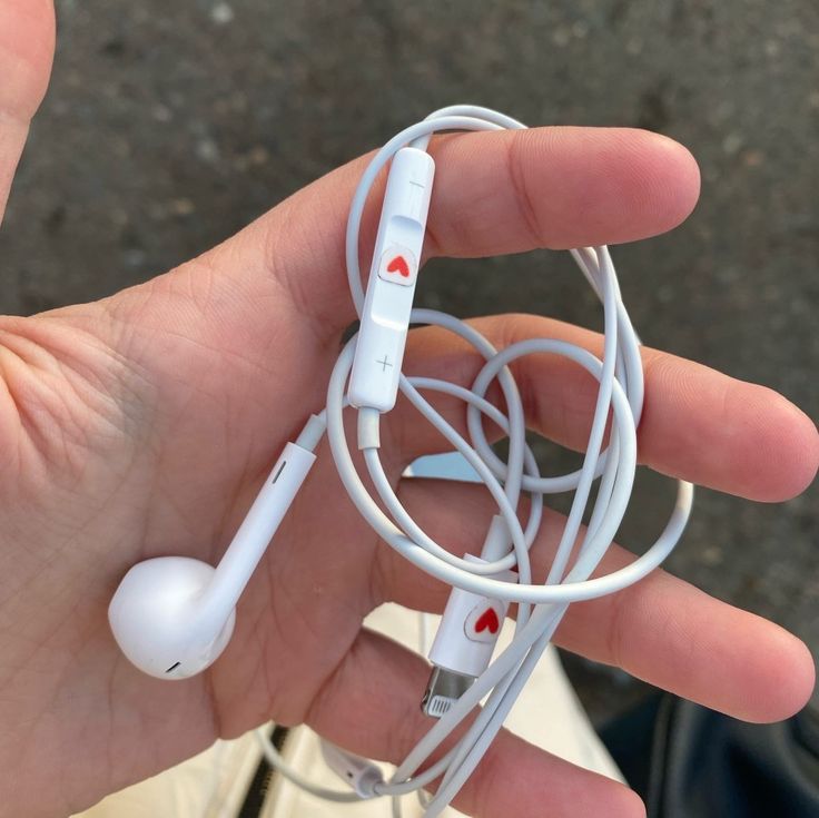 a person is holding an earbud in their left hand and there are two wires attached to the headphones