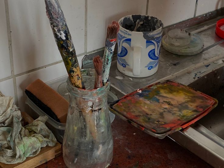 a dirty kitchen counter with paint brushes in a vase