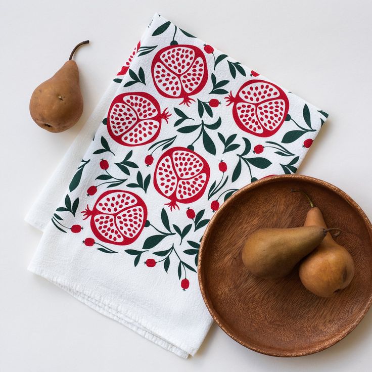 two pears on a wooden plate next to a dish towel with pomegranates