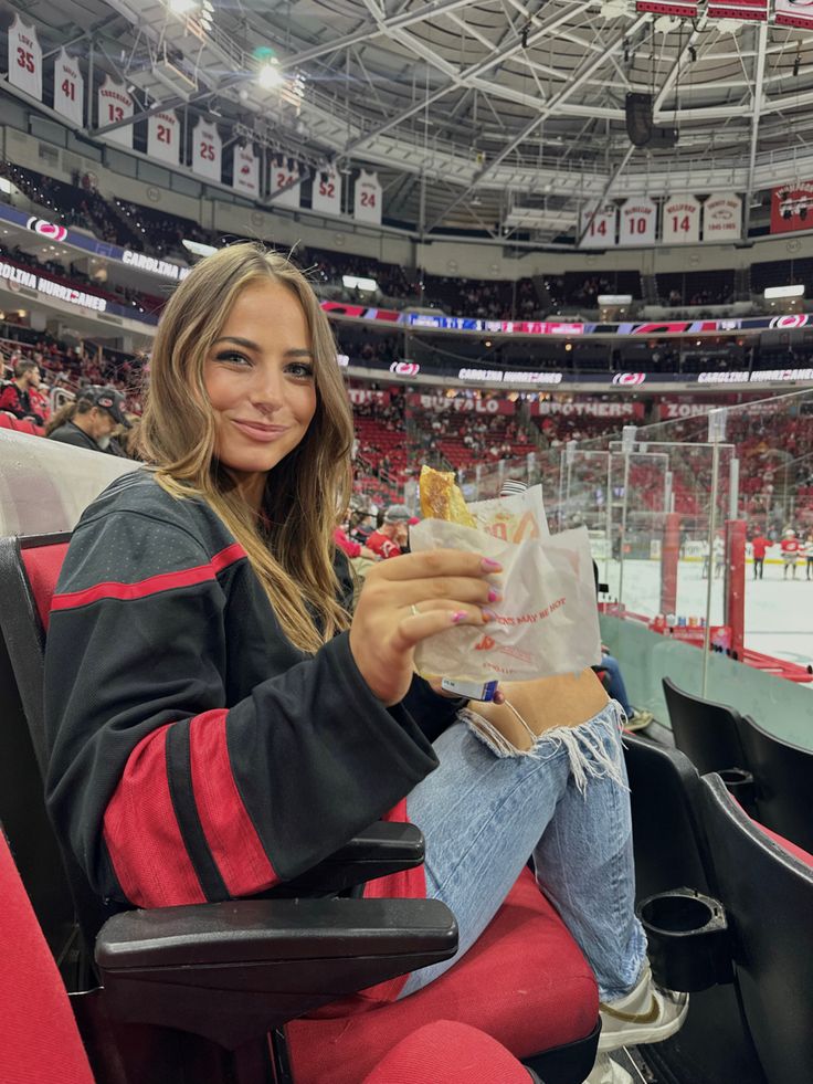 a woman sitting in a chair at an ice hockey game holding a bag of fries