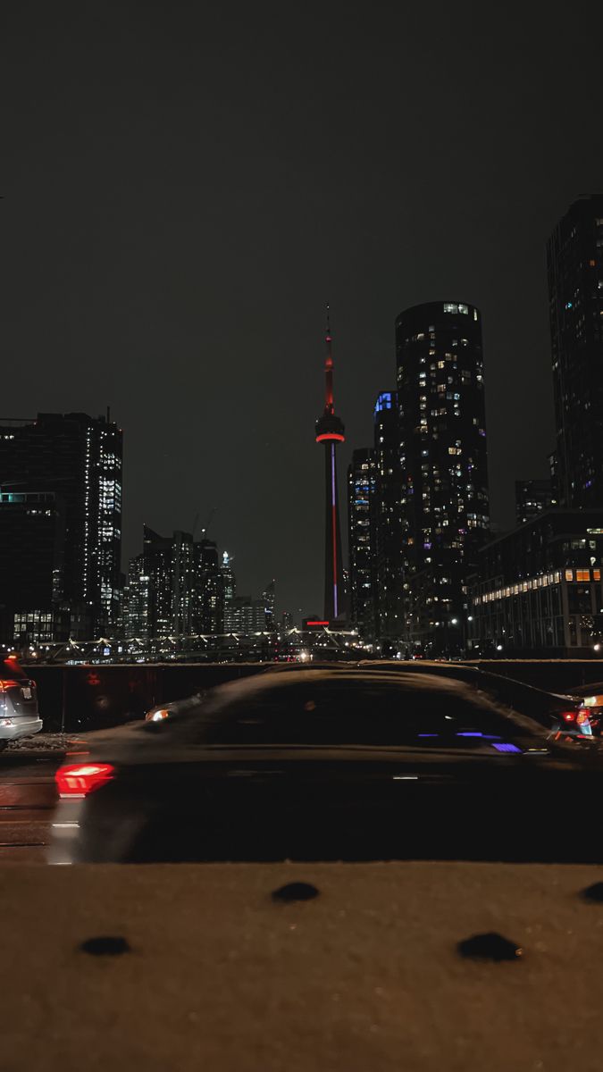 the city skyline is lit up at night, with cars driving on the road in front