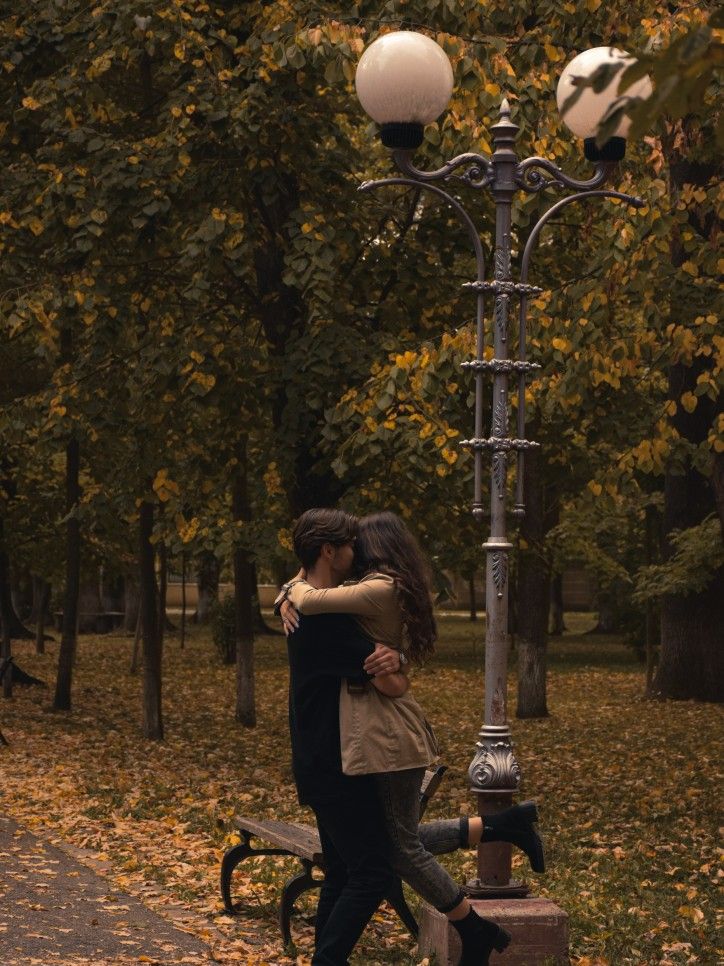 a man and woman hugging under a street light in the park with autumn leaves on the ground