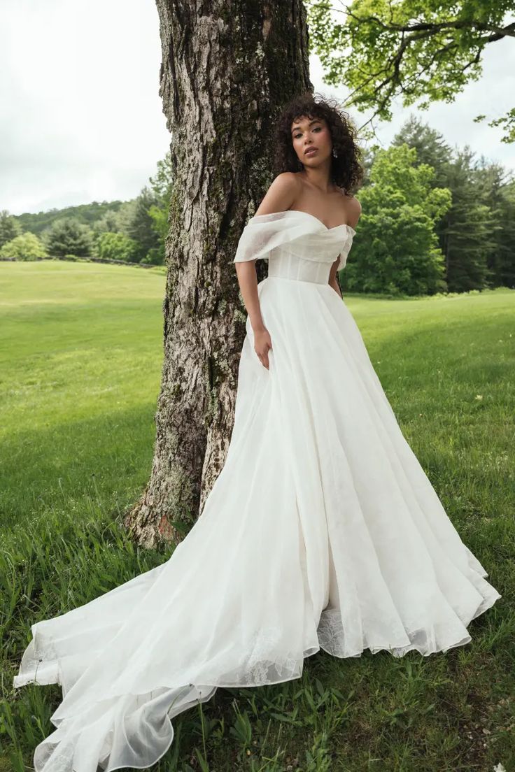 a woman in a wedding dress leaning against a tree