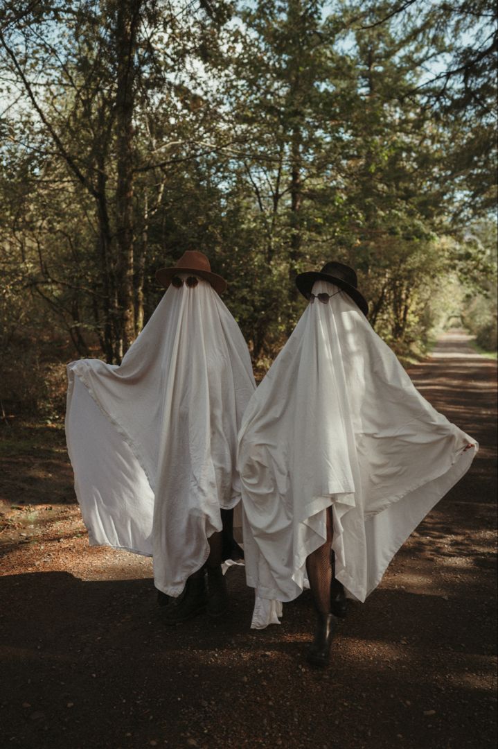 two people in white cloths walking down a dirt road with trees behind their backs