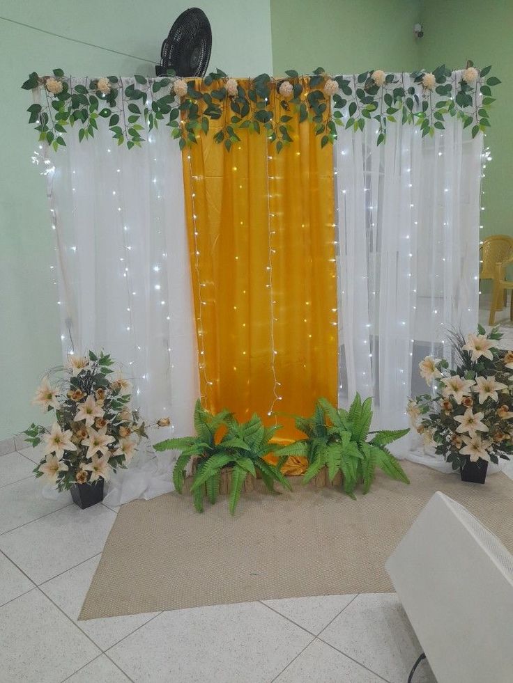 an arrangement of flowers and greenery in front of a yellow curtain