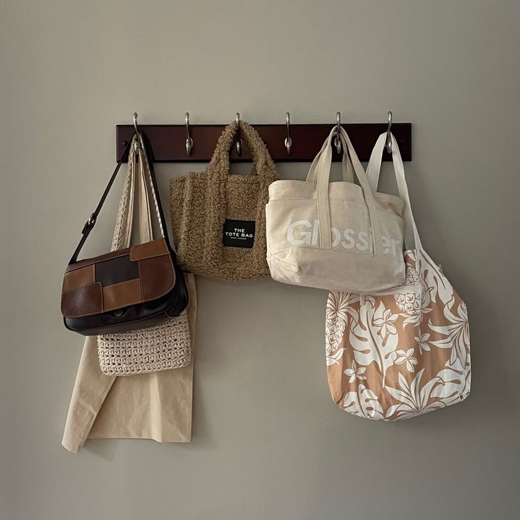 three purses hanging on a coat rack and two totes hanging from the wall