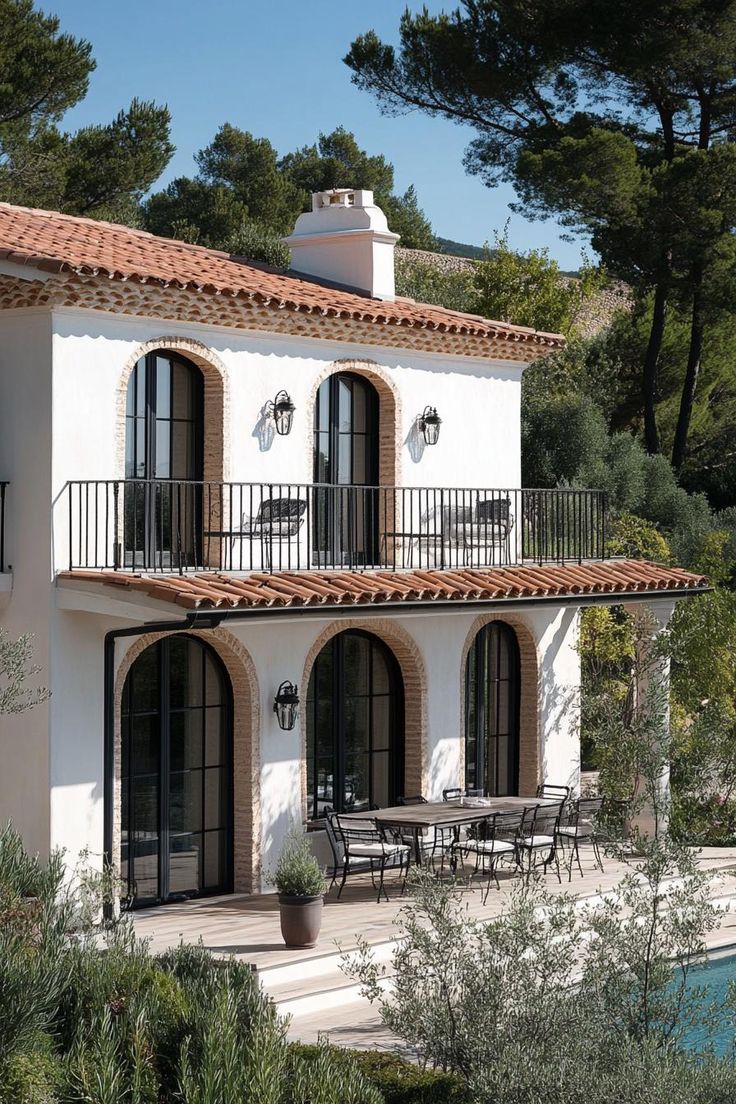 a large white house with two balconies next to a swimming pool and trees