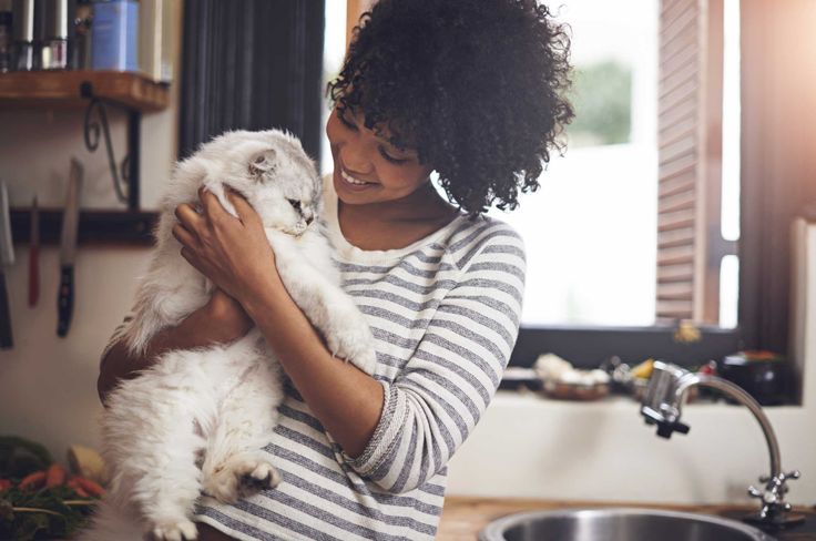 a woman holding a white cat in her arms while standing next to a kitchen sink