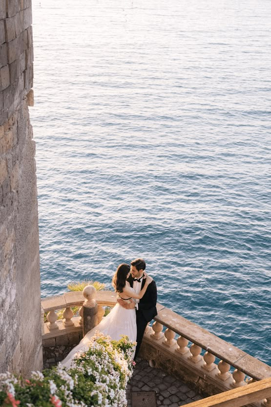 a bride and groom kissing on the steps by the water at their wedding venue in italy