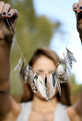 a woman is holding up her hands with feathers hanging from the string in front of her