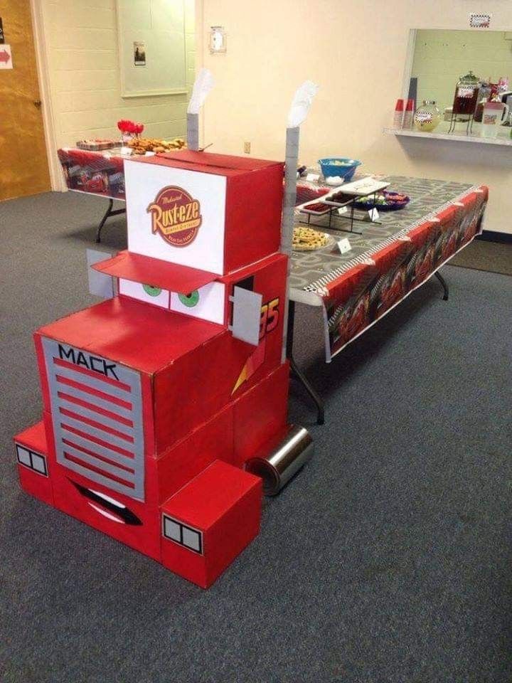 a red truck made out of cardboard sitting on top of a carpeted floor next to a table