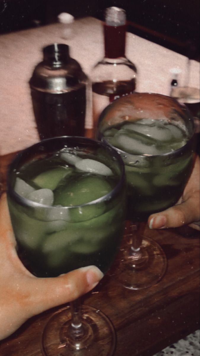 two people holding glasses filled with green liquid