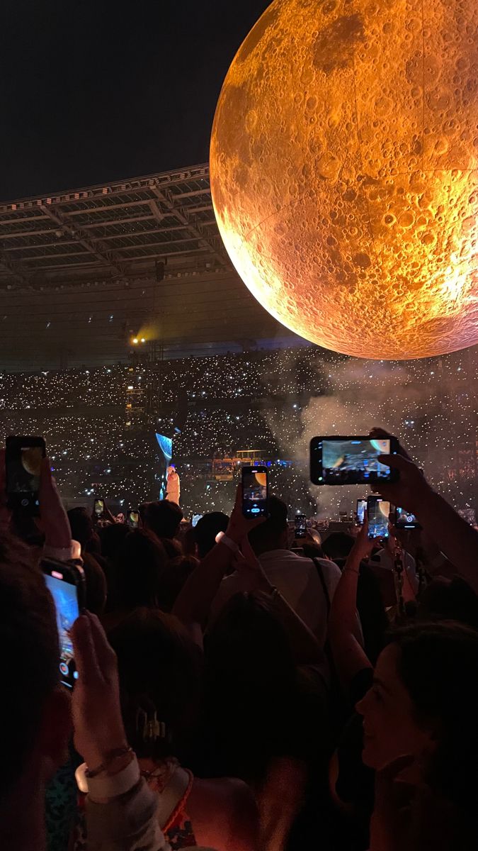 people taking pictures with their cell phones in front of the moon at an outdoor concert