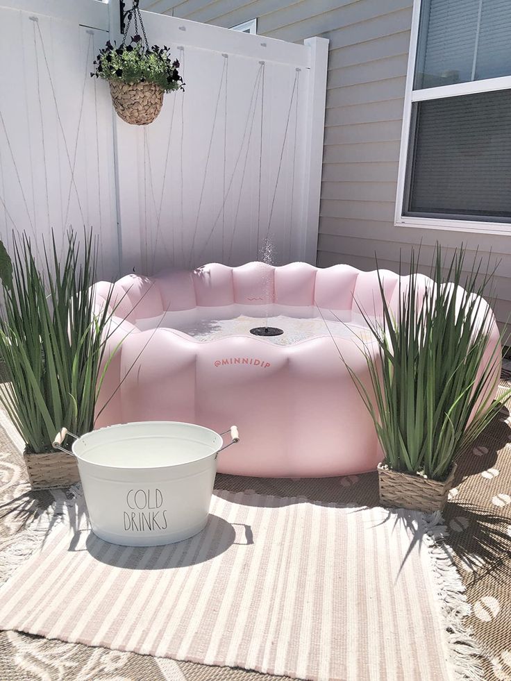 a pink inflatable bathtub sitting on top of a rug next to potted plants