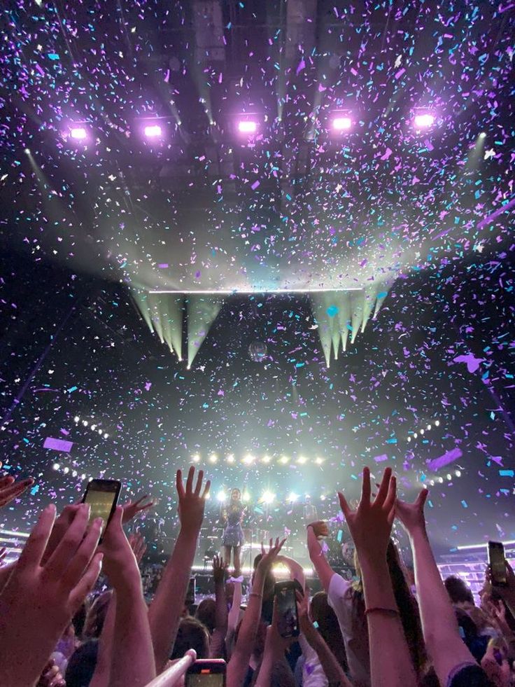 a crowd at a concert with their hands in the air and confetti falling from the ceiling