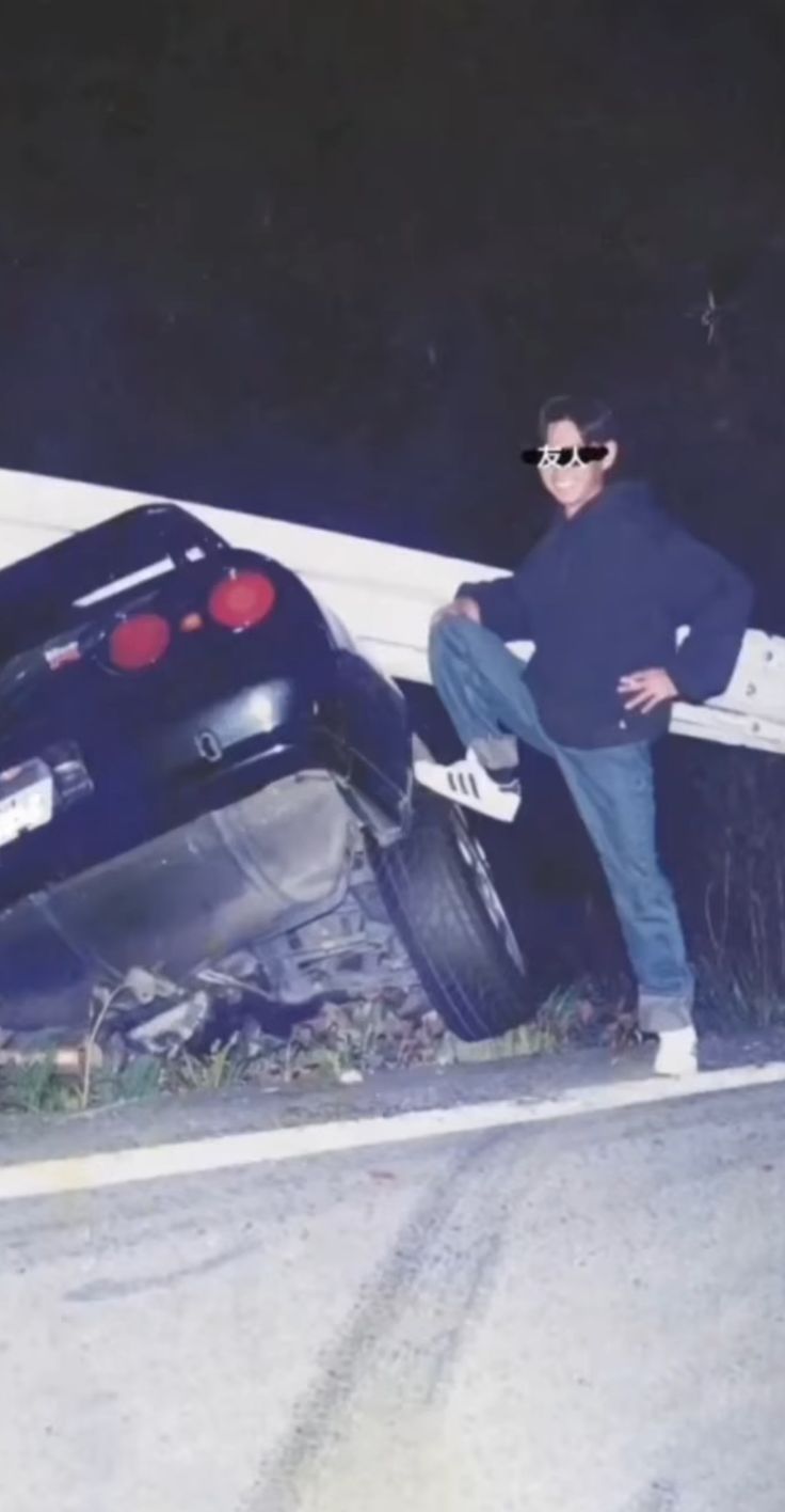 a man standing next to a car that has been flipped over on the side of a road