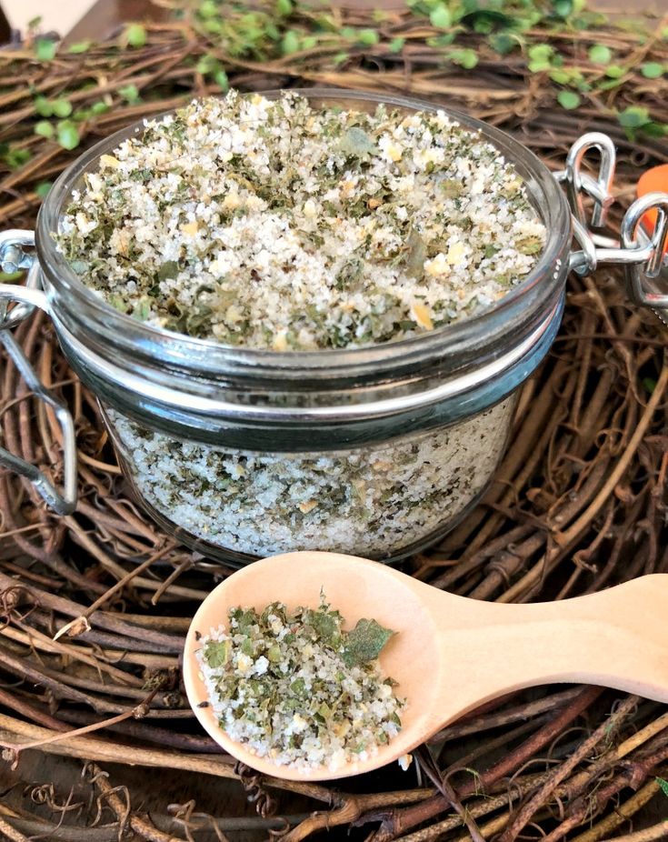 a jar filled with herbs next to a wooden spoon