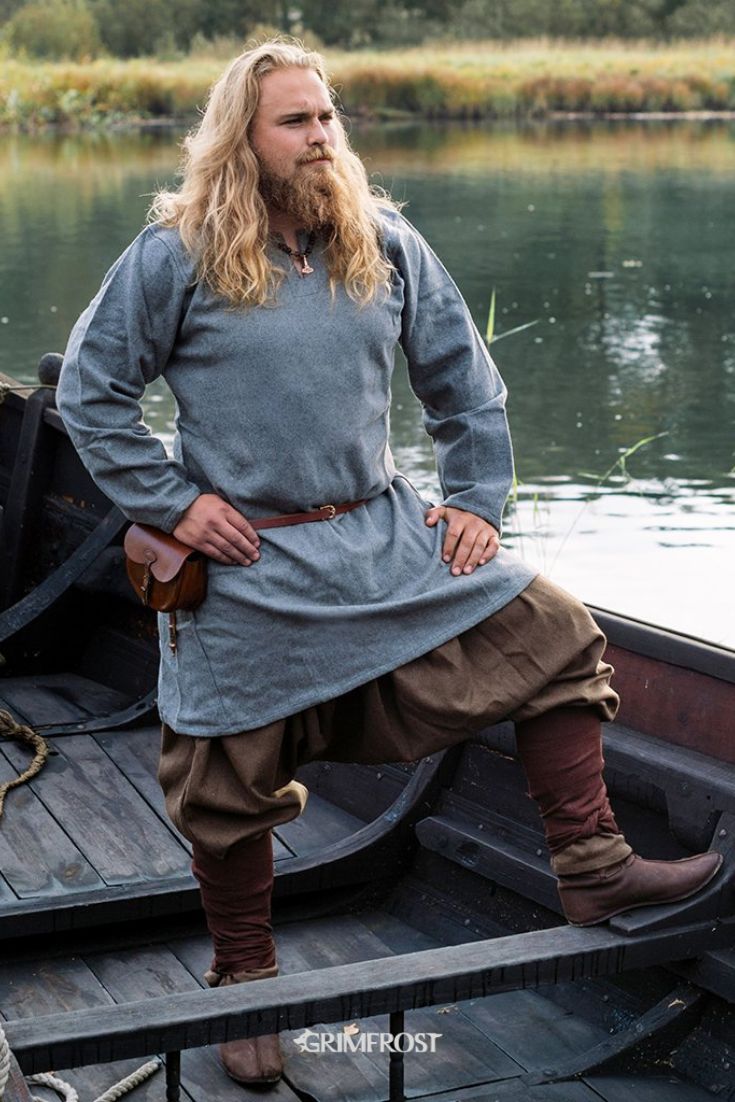 a man with long hair and beard in a gray dress standing on a small boat