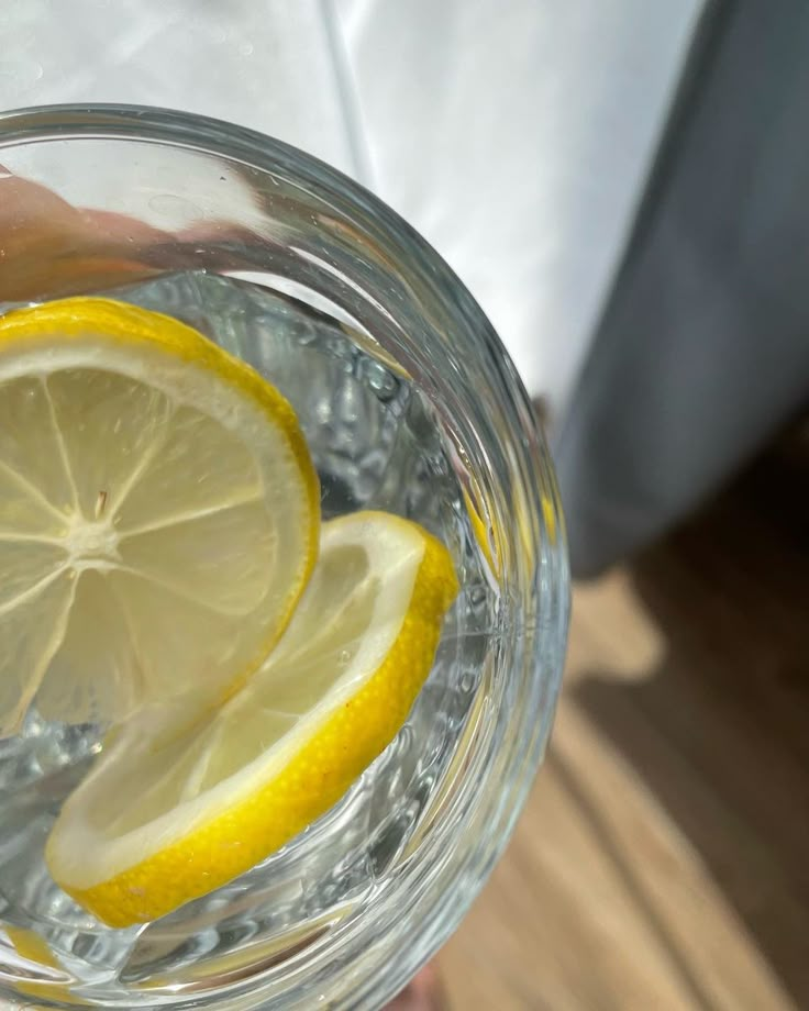 a person holding a glass filled with water and lemon slices