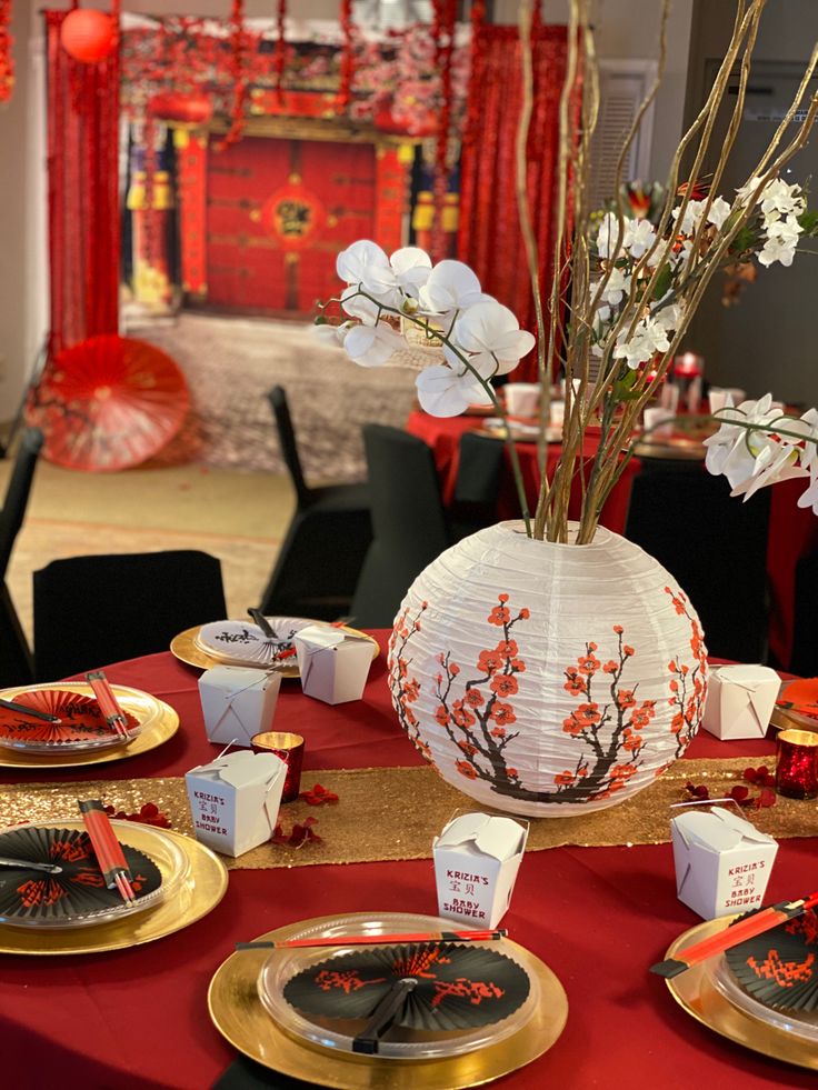 the table is set with red and gold plates, silverware, and paper lanterns