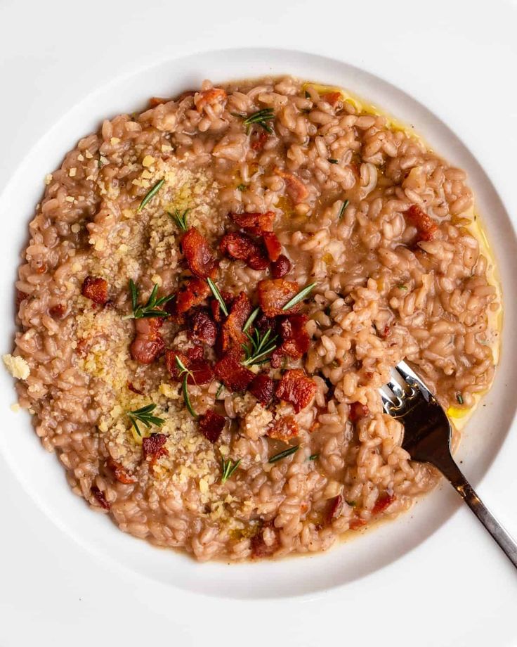 a white plate topped with riso and bacon next to a fork on top of a table