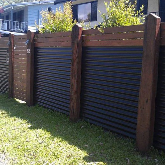 a wooden fence with metal slats and plants growing on it's top, in front of a house