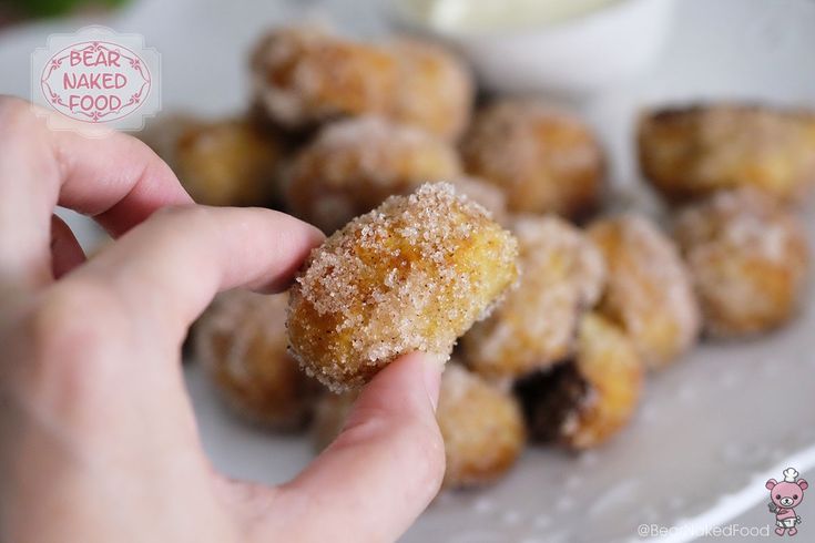 a person holding a sugared donut in their hand with other doughnuts behind them