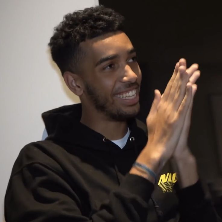 a young man is smiling and clapping his hands in front of the camera while wearing a black hoodie