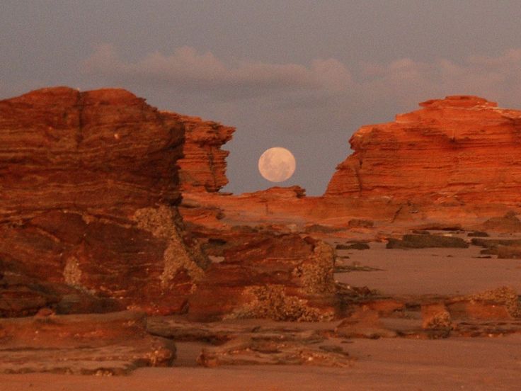 the moon is setting over some red rocks