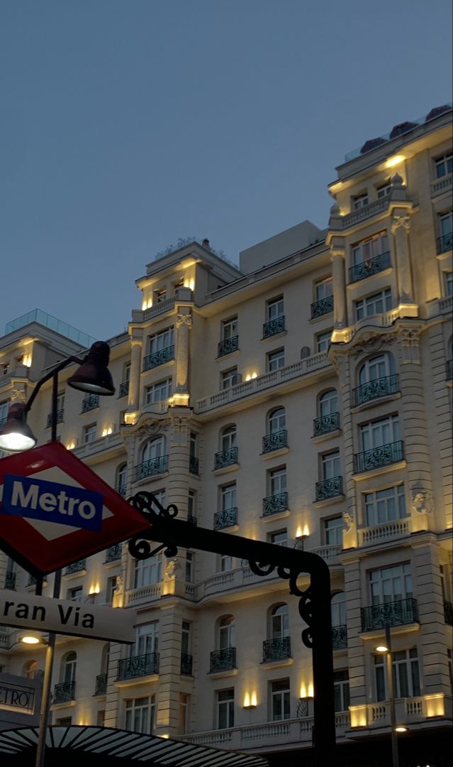 the metro sign is lit up at night in front of a large white building with balconies