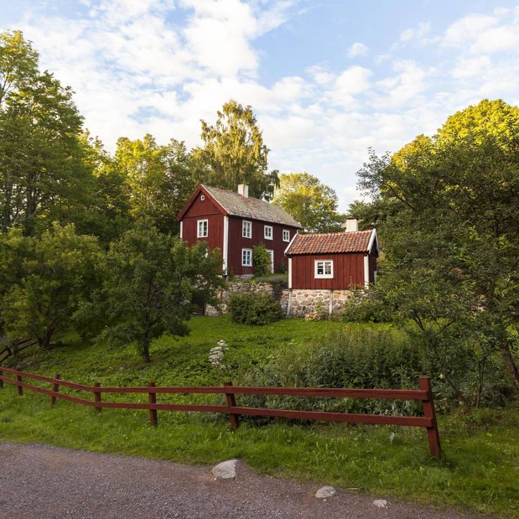 a red house sitting on the side of a lush green hillside next to a forest