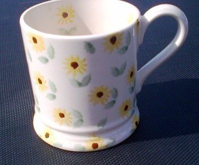 a white coffee cup with yellow and green flowers painted on it sitting on a blue surface