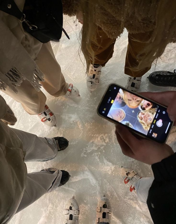 a group of people standing next to each other in the snow looking at a cell phone