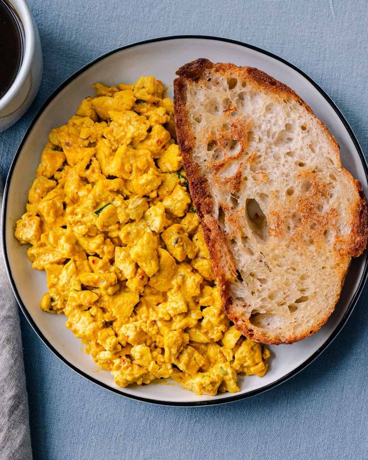 scrambled eggs and toast on a plate next to a cup of coffee