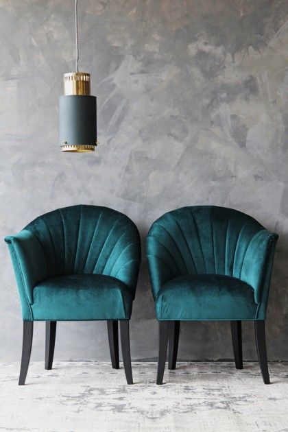 two green velvet chairs in front of a gray wall with a gold pendant light hanging from the ceiling